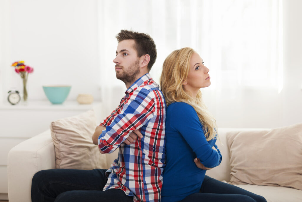 Frustrated couple sitting back-to-back on couch, showing emotional distance in a conflict-heavy marriage