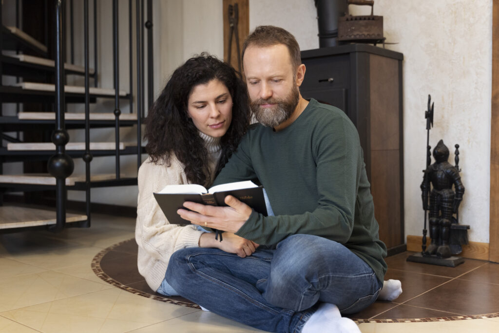 Married couple holding hands in prayer over open Bibles, symbolizing spiritual foundation in marriage