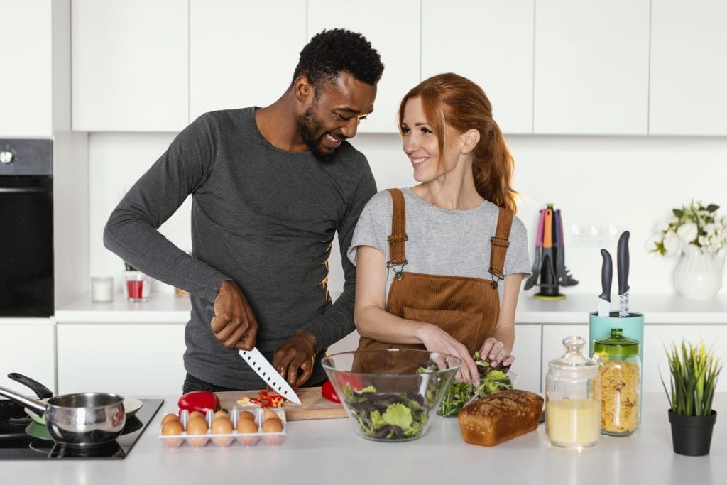 Couple laughing together in kitchen, practicing daily small acts to keep love alive.