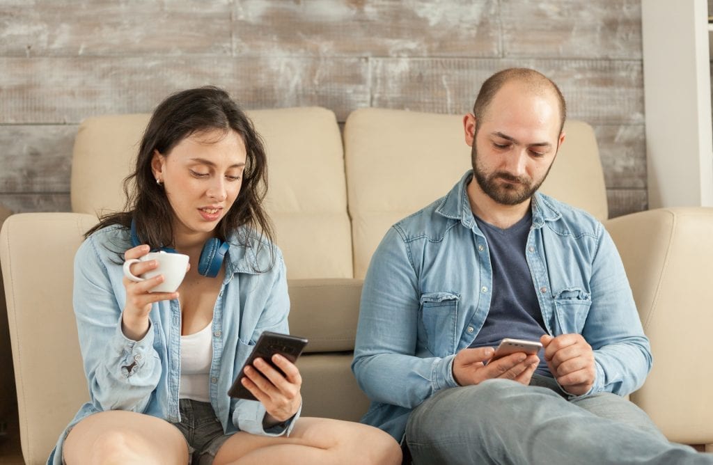 Married couple distracted by phones and disconnected, illustrating cultural habits numbing intimacy
