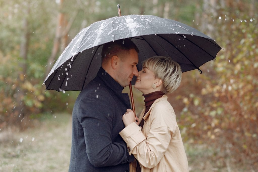 Spouse holding umbrella over both during rainstorm, symbolizing uneven support during heavy seasons of marriage