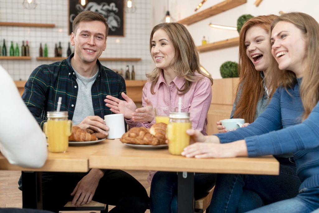 : Couple quietly reflecting as friend group distracts, symbolizing divided loyalties in marriage.