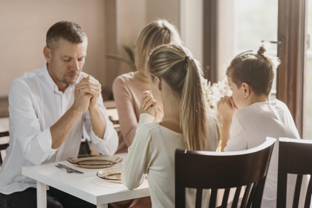 family holding hands around a table during prayer showing shared faith across generations