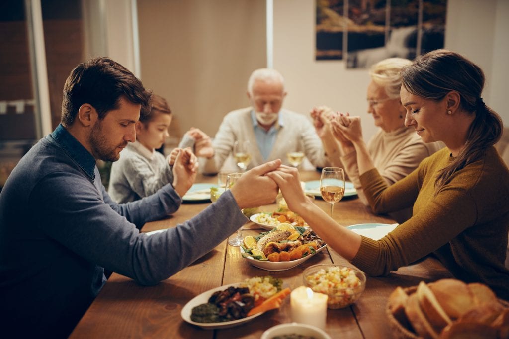 amily praying at dinner table while grandparents watch lovingly, symbolizing faith respect across generations