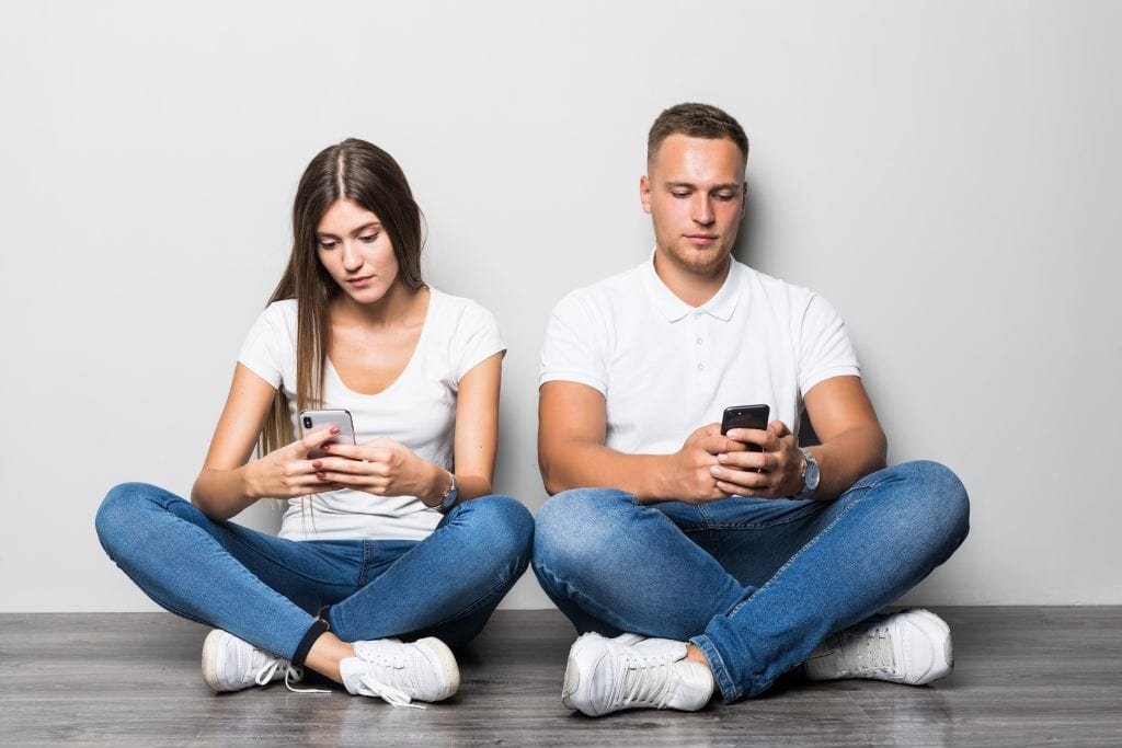 Couple distracted by screens illustrating emotional disconnection.