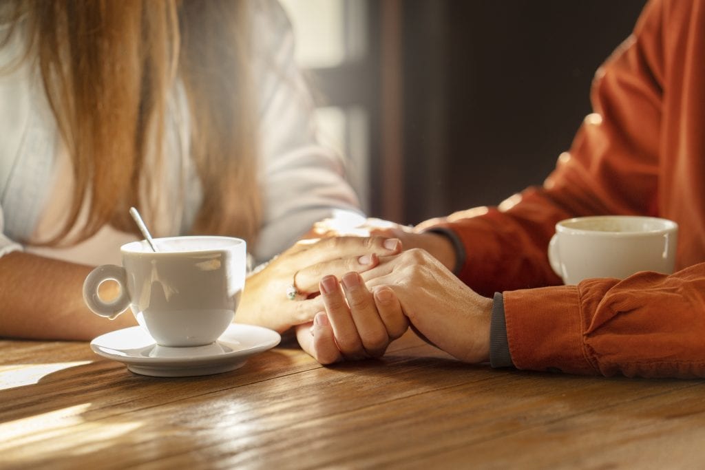 Couple holding hands calmly at a kitchen table after resolving conflict through patience