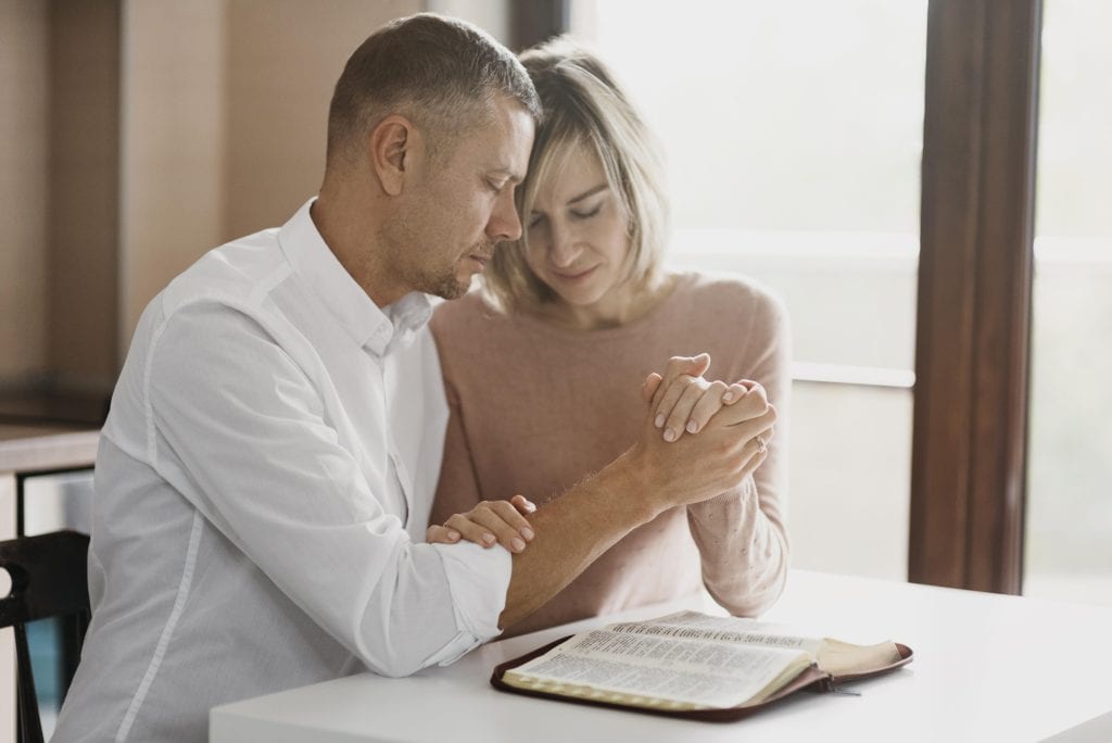Couple holding hands over an open Bible, symbolizing shared faith during long waiting seasons