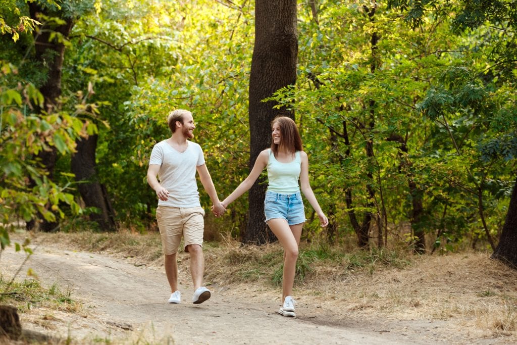 Couple walking through trees symbolizing steady connection through life’s journey.