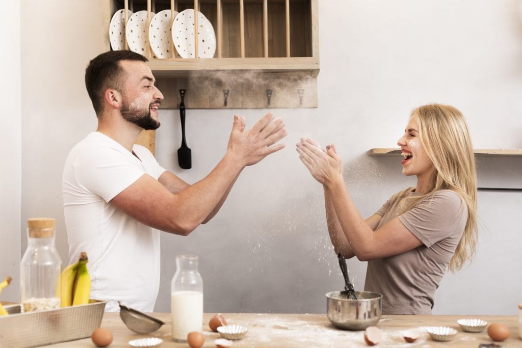 Couple embracing playfulness in marriage by laughing during a kitchen mishap.