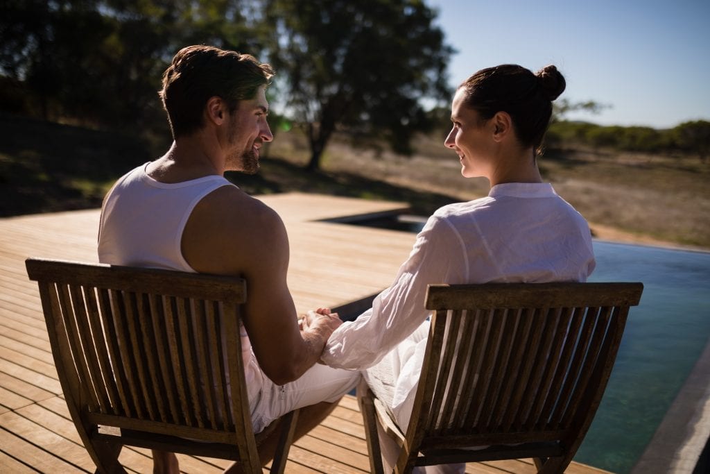Couple sitting close together on a porch at sunset, enjoying the fruits of connection by design in their marriage