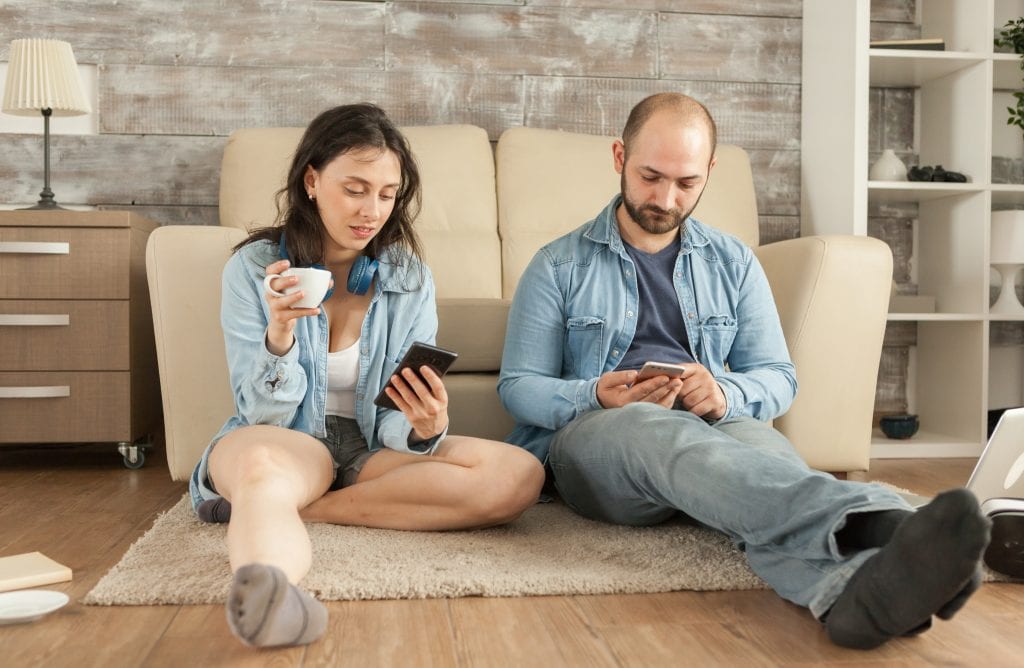 Married couple sitting apart on the couch, distracted on their phones, showing emotional drift before a close call