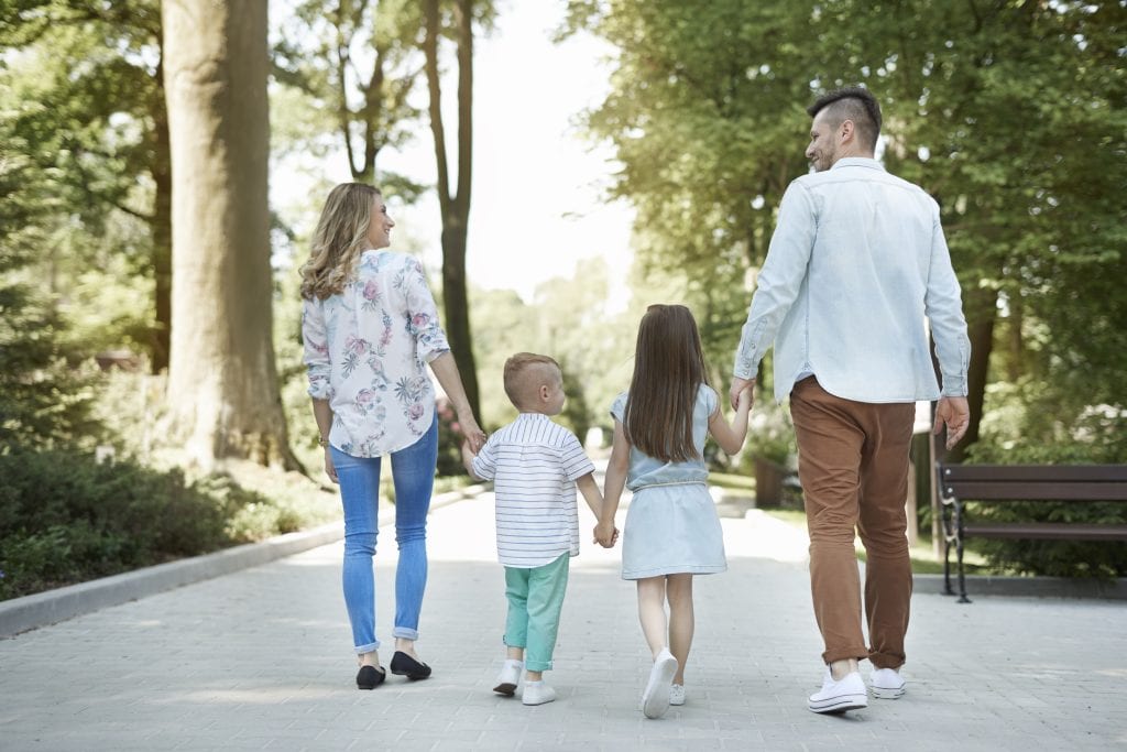 Mom and dad walking hand in hand behind their kids, symbolizing parenting without the power struggle and moving as a united team