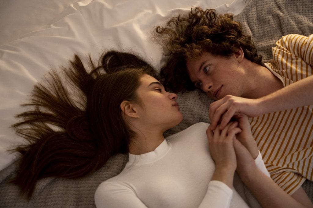 Couple facing each other in bed without phones, showing how simple night-time micro-choices support connection goals